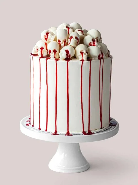 White layer cake piled with white chocolate skulls, red syrup dripping down the sides (The Scran Line)