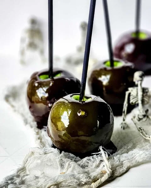 Glossy black candy apples on black sticks, with green apple showing at the top (Everyday Eileen)